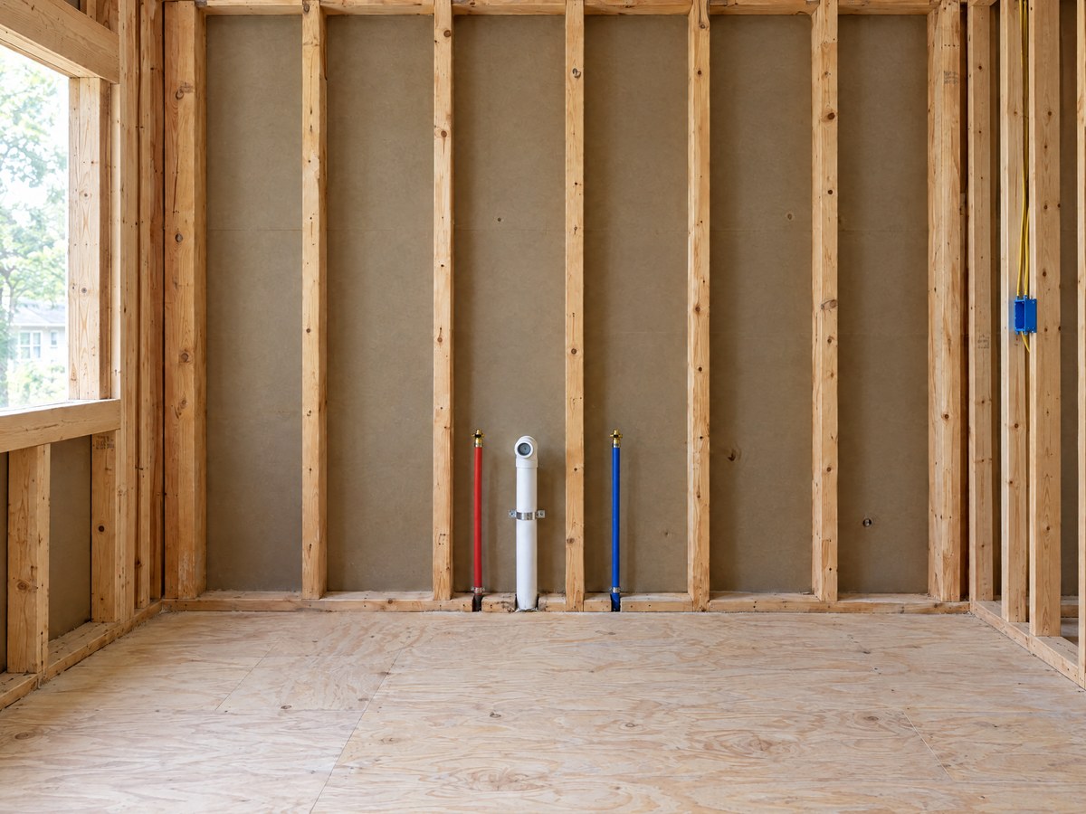 Illustration: the same kitchen sink wall open to the studs, with the drain and the hot and cold supply lines
